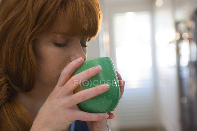 Frau trinkt Kaffee im grünen Becher zu Hause — Stockfoto