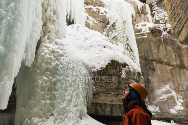 Скалолаз зимой смотрит на скалистую ледяную гору — стоковое фото
