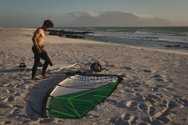 Surfeur masculin debout avec cerf-volant et planche de surf sur la plage au crépuscule — Photo de stock