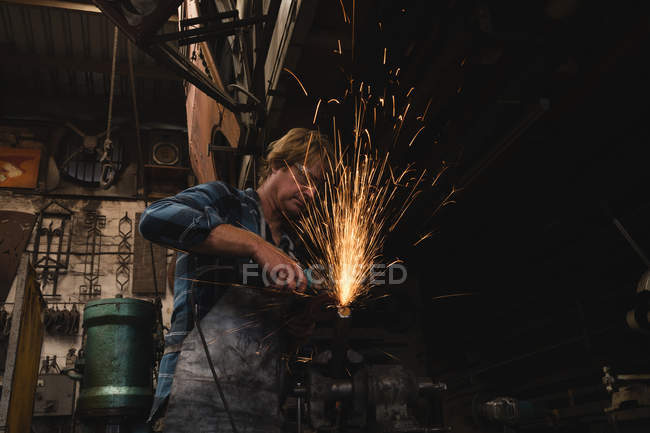 Blacksmith grinding a metal rod with grinder machine n workshop — Stock Photo