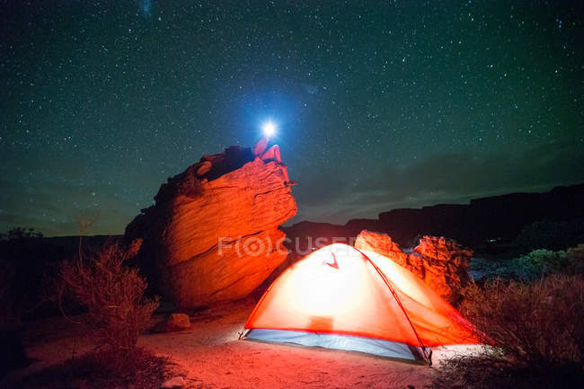 Мужской турист на скале возле палатки в сельской местности ночью — стоковое фото