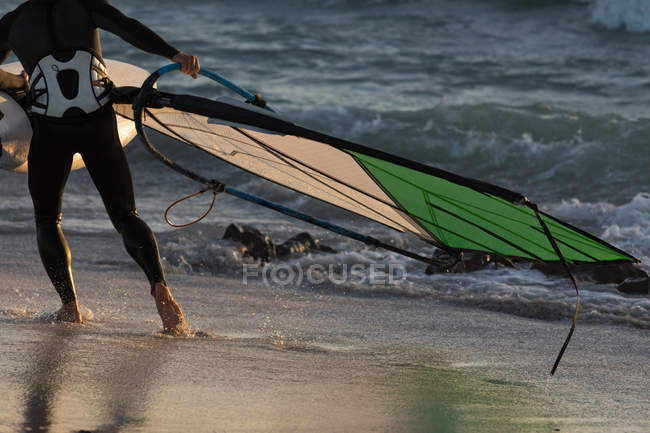 Surfista maschio che tiene un aquilone sulla spiaggia al crepuscolo — Foto stock
