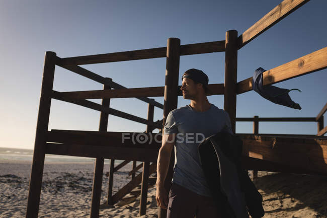 Pensativo surfista masculino de pie en la playa - foto de stock