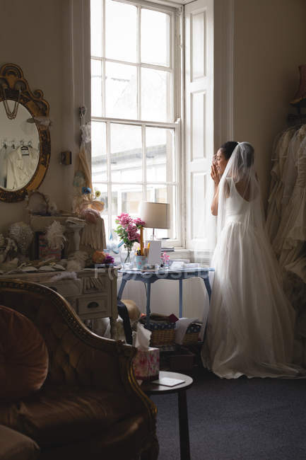 Жінка змішаної раси, наречена в білій сукні дивиться через вікно на старовинному бутіку — стокове фото