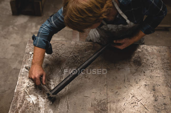 Forgeron mesurant une tige métallique avec étrier en atelier — Photo de stock