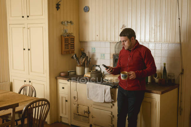 Чоловік тримає бездротовий телефон, маючи каву вдома — стокове фото