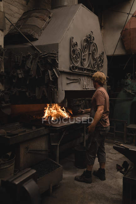 Blacksmith heating metal rod in fire at workshop — Stock Photo