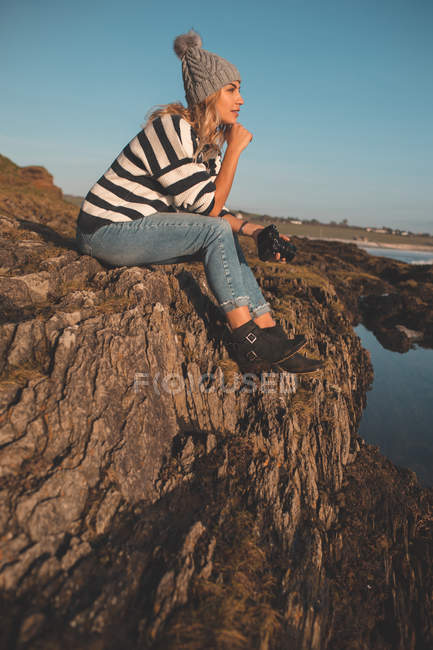 Nachdenkliche Frau sitzt am Strand auf einem Felsen — Stockfoto