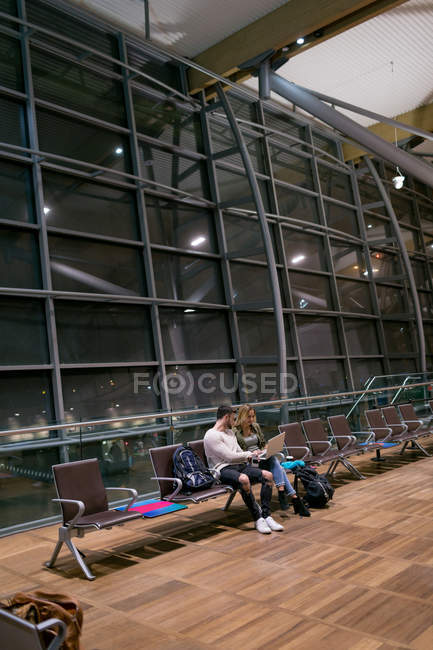 Casal usando laptop na área de espera no aeroporto — Fotografia de Stock
