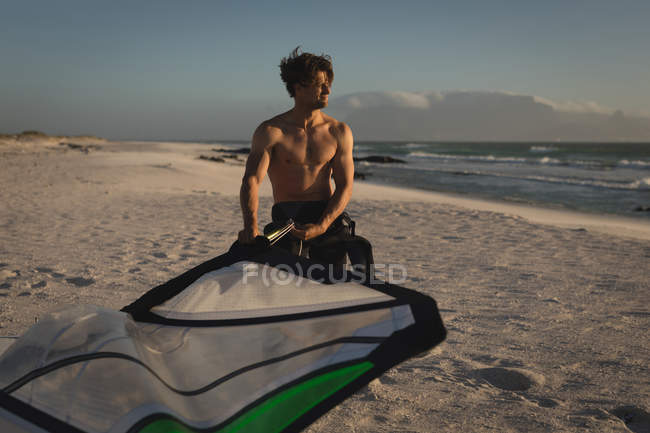 Мужчина-серфер держит воздушного змея на пляже в сумерках — стоковое фото