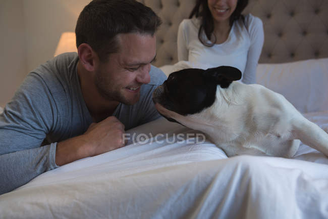Couple jouer avec leur chien de compagnie dans la chambre à coucher à la maison — Photo de stock