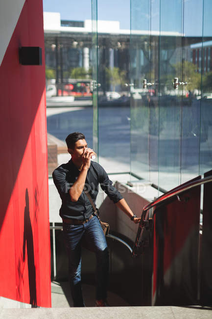 Jovem empresário se movendo no andar de cima enquanto toma café — Fotografia de Stock