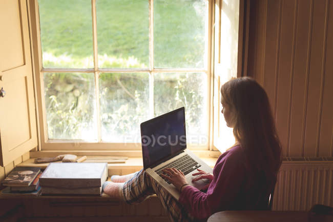 Женщина с ноутбуком возле окна дома — стоковое фото