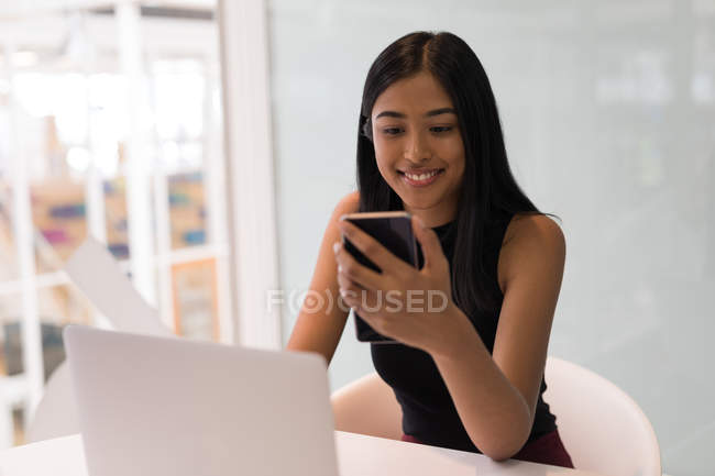 Молода жінка виконавча з використанням мобільного телефону в офісі — стокове фото