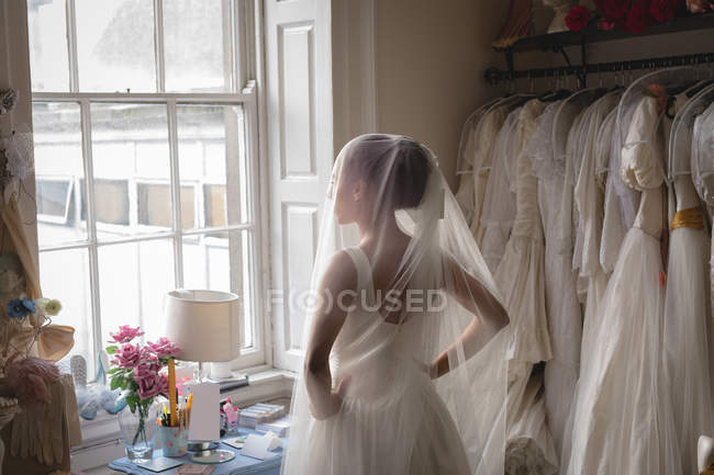Femme métisse, mariée en robe blanche regardant par la fenêtre à la boutique vintage — Photo de stock