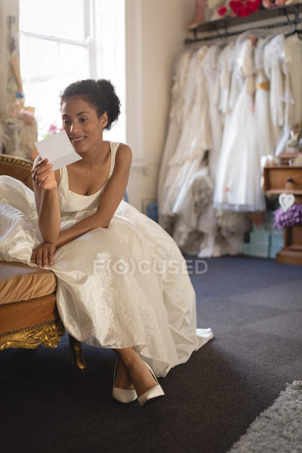 Молодая невеста в свадебном платье читает записку, сидя на диване — стоковое фото