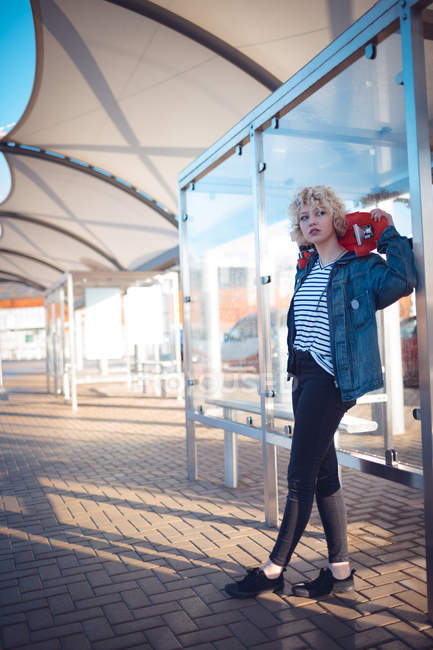 Молода жінка тримає скейтборд на автобусній зупинці — стокове фото