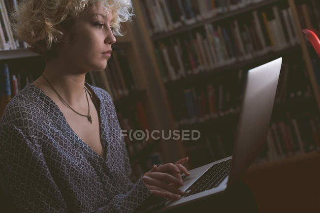 Giovane donna che utilizza il computer portatile in biblioteca — Foto stock