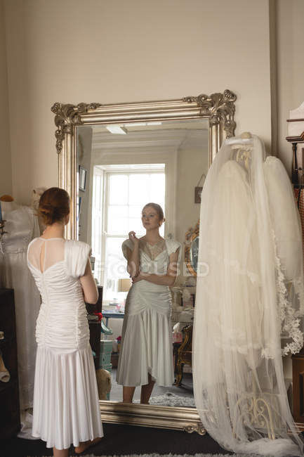 Caucasian bride in wedding dress looking into mirror at vintage boutique — Stock Photo