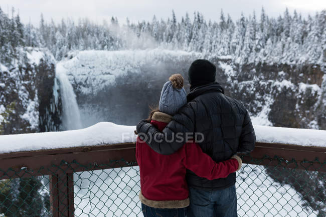 Paar in warmer Kleidung schaut sich im Winter Wasserfall an — Stockfoto