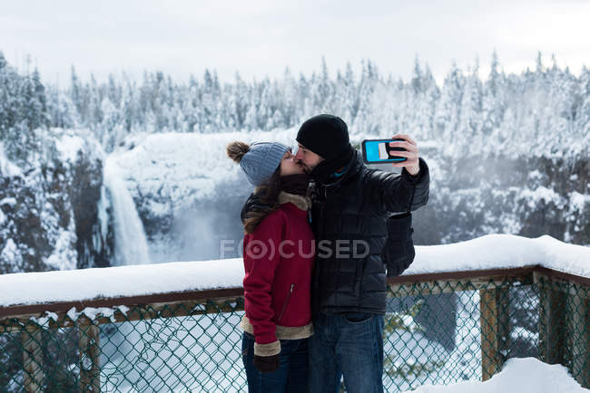 Пара бере селфі з мобільним телефоном біля водоспаду взимку — стокове фото
