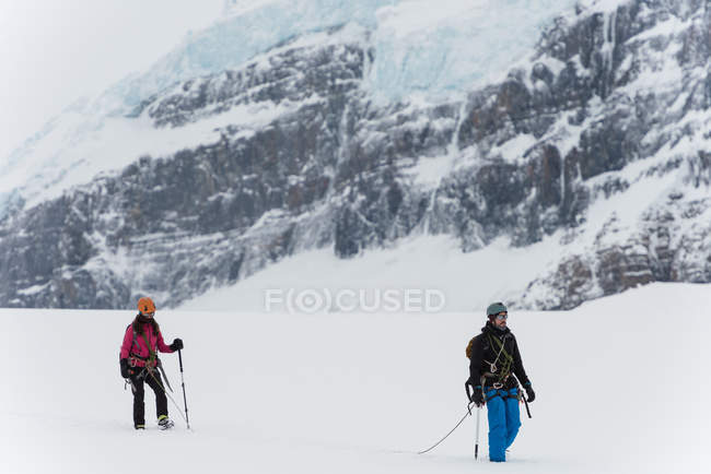 Caminhada de casal com arnês em uma montanha coberta de neve durante o inverno — Fotografia de Stock