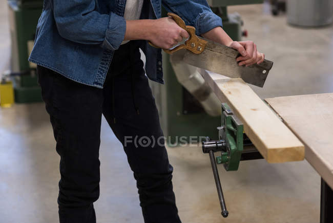 Средняя часть женского плотника с помощью ручной пилы в мастерской — стоковое фото