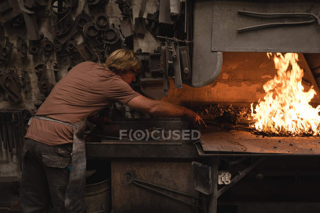 Ferreiro de aquecimento haste de metal em fogo na oficina — Fotografia de Stock