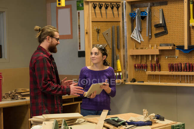 Carpinteros masculinos y femeninos discutiendo sobre tableta digital en taller - foto de stock