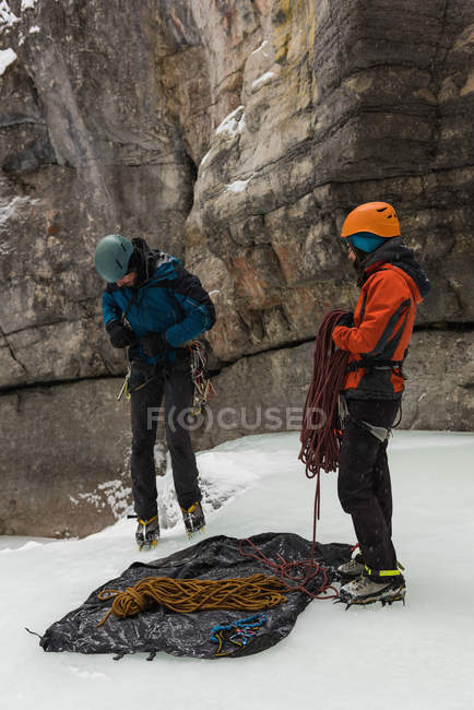 Scalatore maschio che indossa un'imbracatura vicino alla montagna rocciosa durante l'inverno — Foto stock