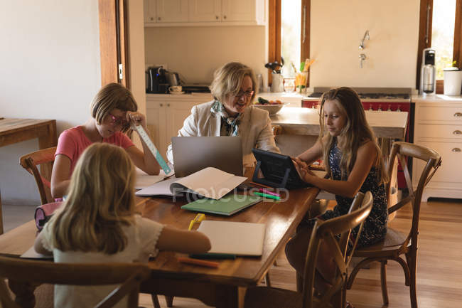 Mother using laptop while children dosing their homework at home — Stock Photo