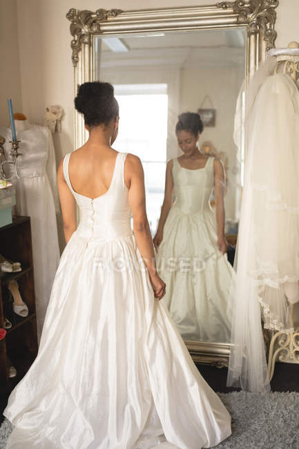 Молода наречена у весільній сукні дивиться у дзеркало в бутіку — стокове фото