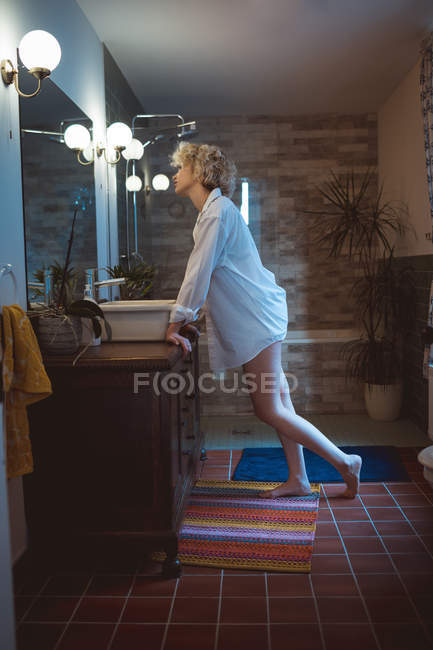 Young woman looking in mirror at bathroom — Stock Photo