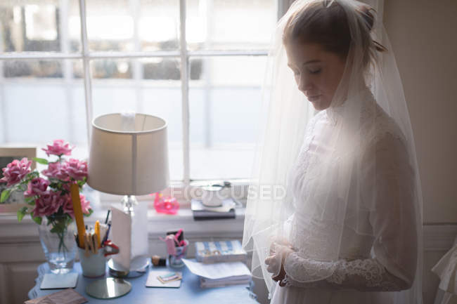 Jeune mariée en robe de mariée debout près de la fenêtre à la boutique — Photo de stock