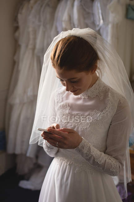 Кавказская невеста в свадебном платье с помощью мобильного телефона в бутике — стоковое фото