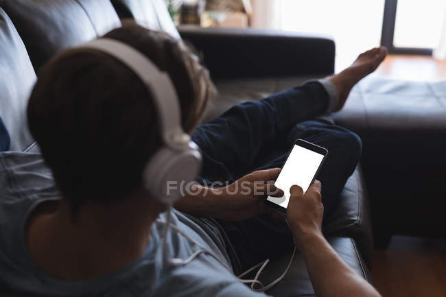 Homem usando telefone celular com fones de ouvido na sala de estar em casa — Fotografia de Stock
