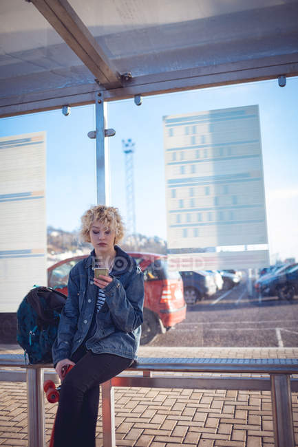 Jeune femme utilisant un téléphone portable à l'arrêt de bus — Photo de stock