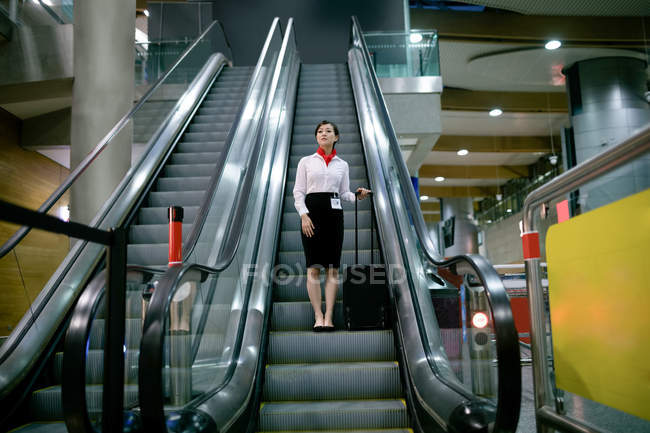 Mujer parada en escalera mecánica con equipaje en el aeropuerto - foto de stock