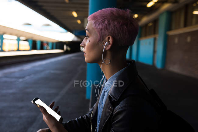 Стильна жінка слухає музику на мобільному телефоні на залізничній станції — стокове фото
