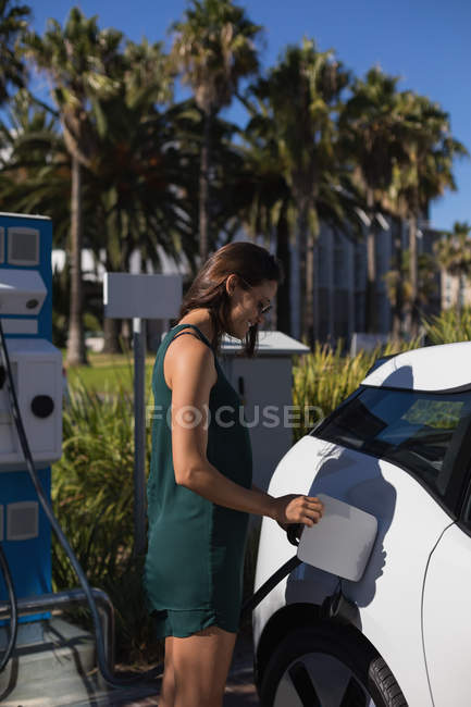 Belle femme recharge voiture électrique à la station de charge — Photo de stock
