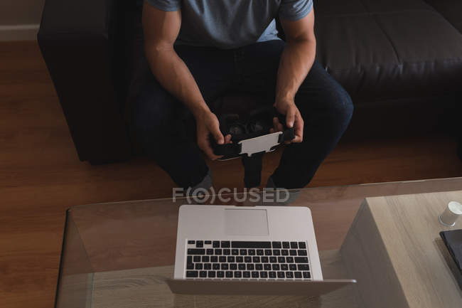 Homem segurando fone de ouvido realidade virtual na sala de estar em casa — Fotografia de Stock