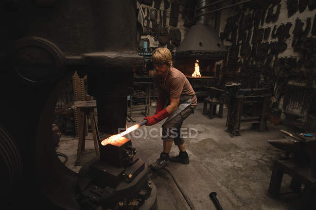 Blacksmith shaping hot metal rod in machine at workshop — Stock Photo