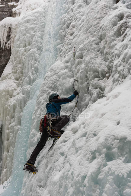 Scalatore di roccia maschile arrampicata montagna di ghiaccio durante l'inverno — Foto stock