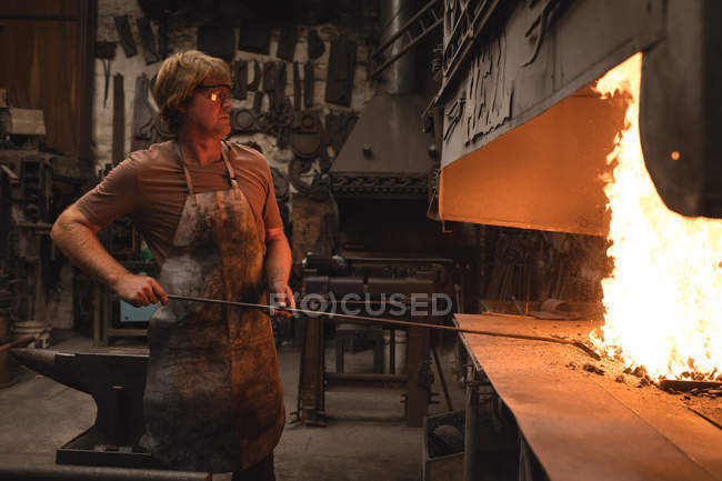 Blacksmith heating metal piece in fire at workshop — Stock Photo