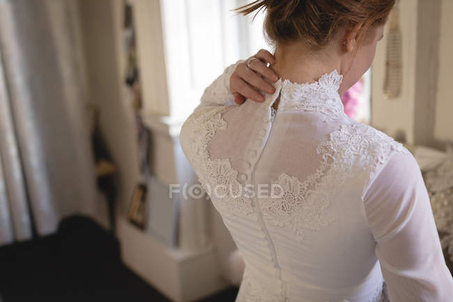 Rear view of bride adjusting button on back of wedding dress in boutique — Stock Photo
