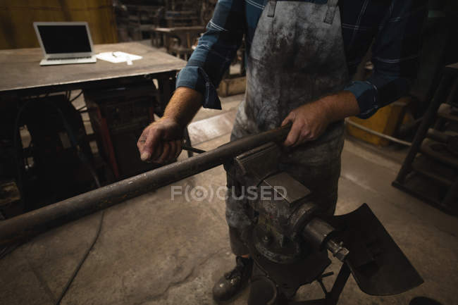 Blacksmith tightening metal rod in workshop — Stock Photo