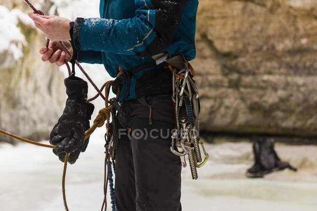 Escalador masculino em pé perto de montanha de gelo rochosa durante o inverno — Fotografia de Stock