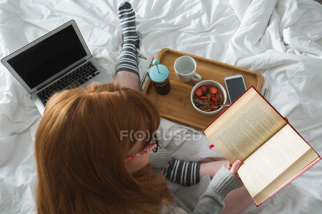 Mujer leyendo un libro en el dormitorio en casa - foto de stock