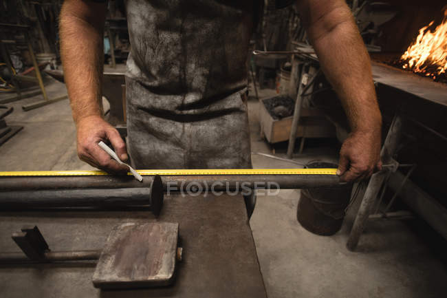 Кузнец измеряет металлический стержень с помощью измерительной ленты — стоковое фото