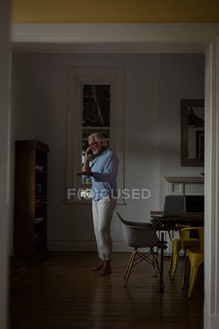 Homme âgé actif parlant sur un téléphone portable à la maison — Photo de stock